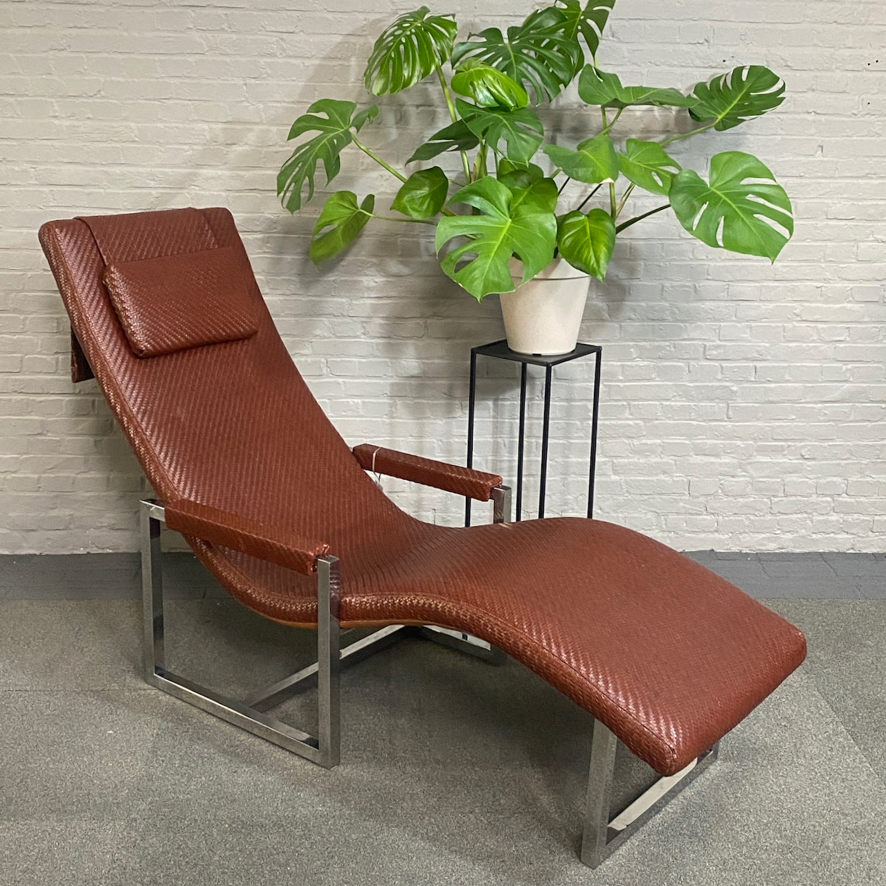 Ein brauner Loungesessel neben einer grünen Pflanze vor einer hellen Backsteinwand