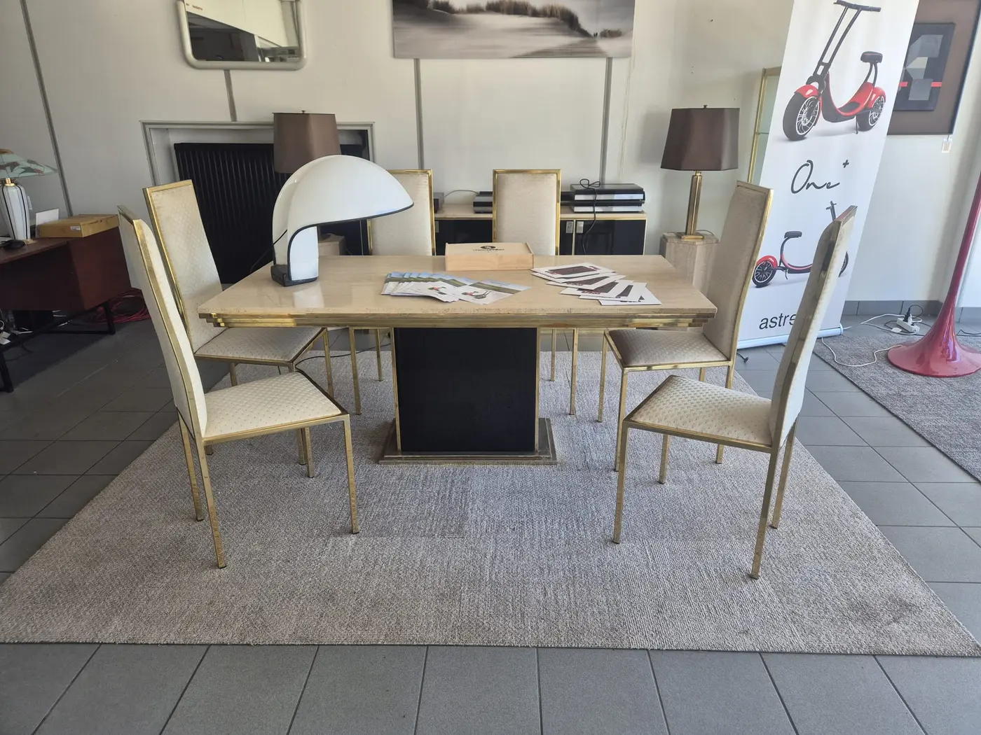 Een lichte eettafel met stoelen onder een groep lampen in een showroom van Claudia Collections