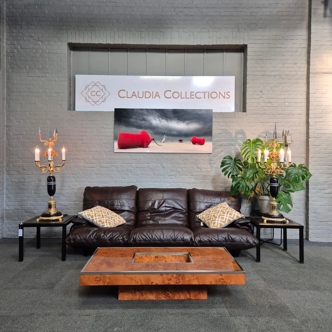 Een bruine bank, houten salontafel en kandelaars onder een bord van Claudia Collections